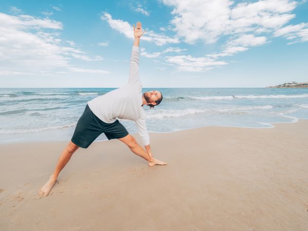 Man training yoga on beach