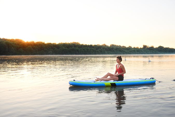 Woman sitting on paddle board in the middle of a lake