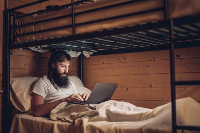 Man using laptop in rustic bunk bed
