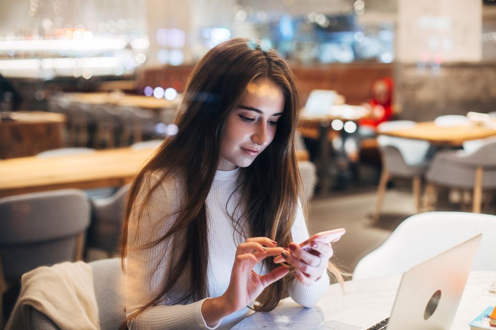 Young brunette woman texting while working on her laptop
