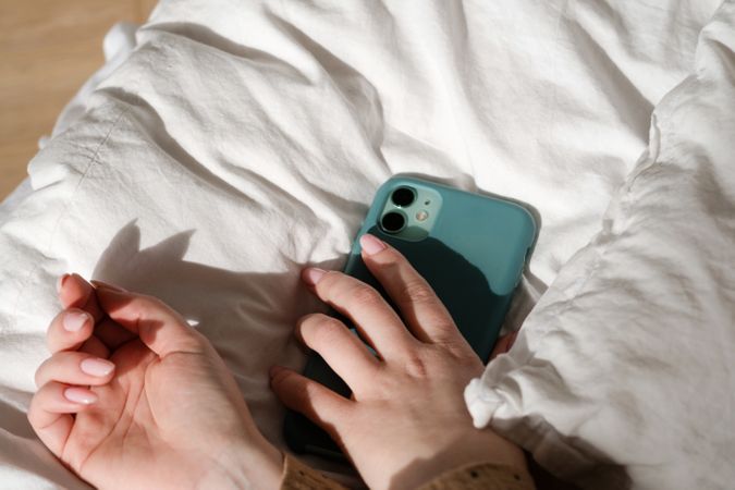 Hand holding smartphone on bed