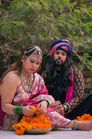 Indian woman wearing floral dress holding flowers sitting beside a man on ground