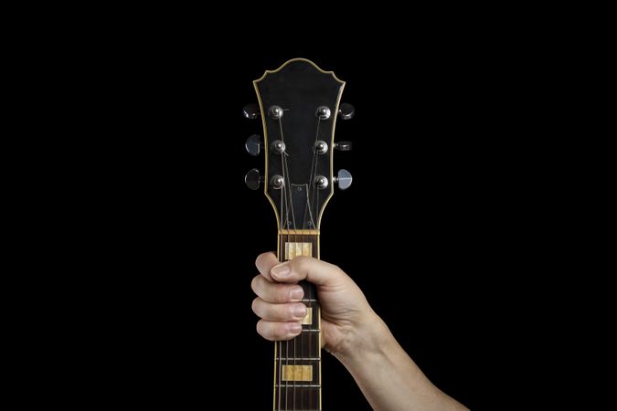 Hand gripping the neck of an electric guitar on a dark background.