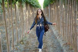 A Joyful and Radiant Young Woman Walking Happily in Nature Among Tall Trees and Greenery