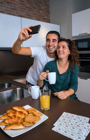 Smiling couple in pajamas taking selfie in kitchen at breakfast time