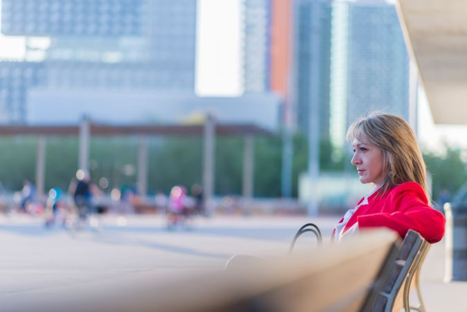 Elegant woman in red jacket sitting on a bench outdoors while deep in thought