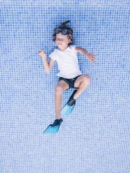 Excited preteen boy on bottom of empty pool imagining swimming