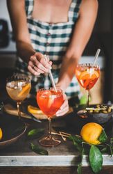 Young woman in checkered dress stirring aperitif with orange slices