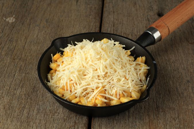 Cast iron pan for sweet corn and grated cheese on wooden table