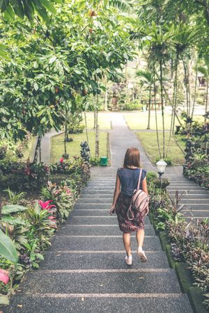 Back view of young woman with bag walking down concrete steps in a garden