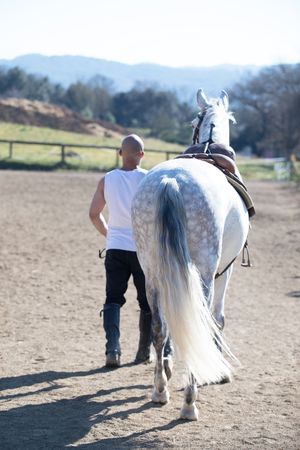 Rear view of a man walking with his horse around paddock