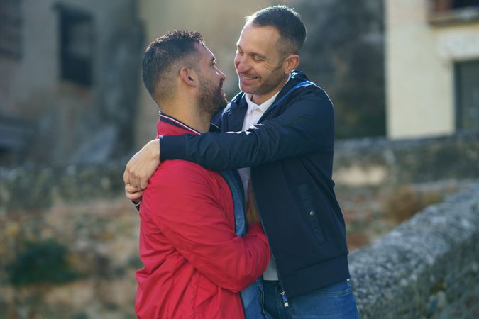Two men hugging embracing near stone wall outside