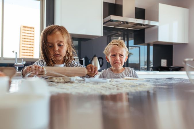 Little girl with rolling pin and flour with her brother crying in kitchen