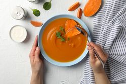 Looking down at person eating bowl of sweet potato soup on table with napkin