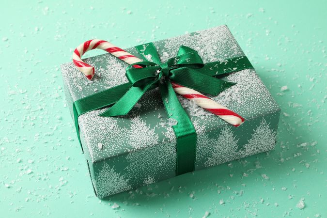 Christmas box with candy cane on mint background with snow