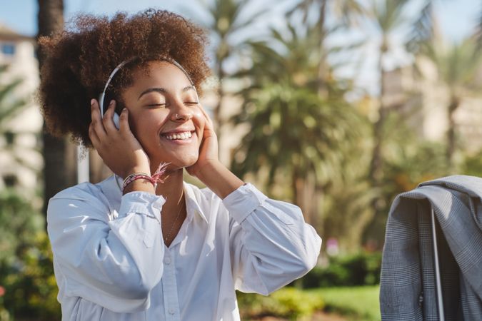Positive Black female in white shirt listening to music on street