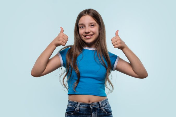 Young girl in blue top confidently gives a thumbs-up.