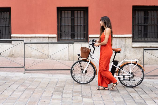 A Stylish Woman in a Vibrant Red Dress Walks by Her ebike Near a Colorful Artistic Wall