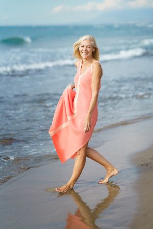 Vertical composition of laughing mature woman walking along the coast
