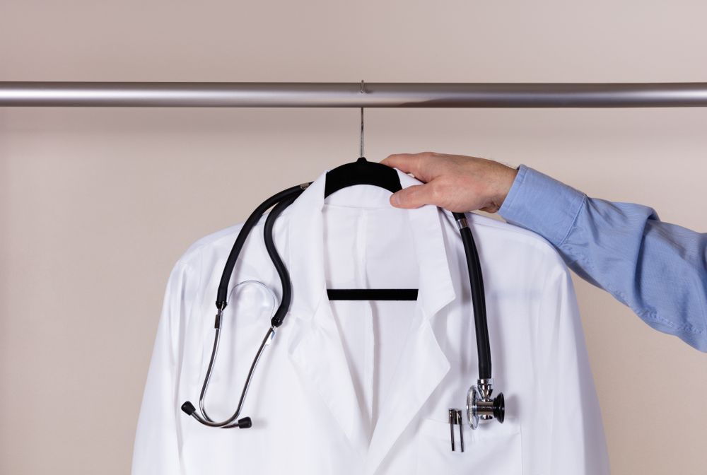 Medical consultation coat with stethoscope being taken off rack by male doctor hand