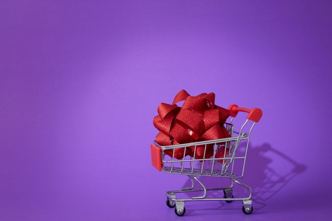 Shopping Cart with Decorative Red Ribbon on Purple Background