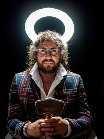 Serious man with glowing fake nimbus holding mirror and looking at camera