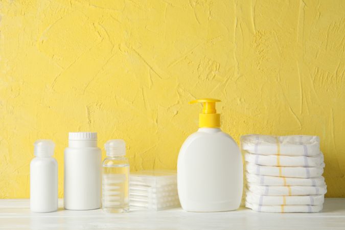 Baby hygiene accessories on wooden table against yellow background