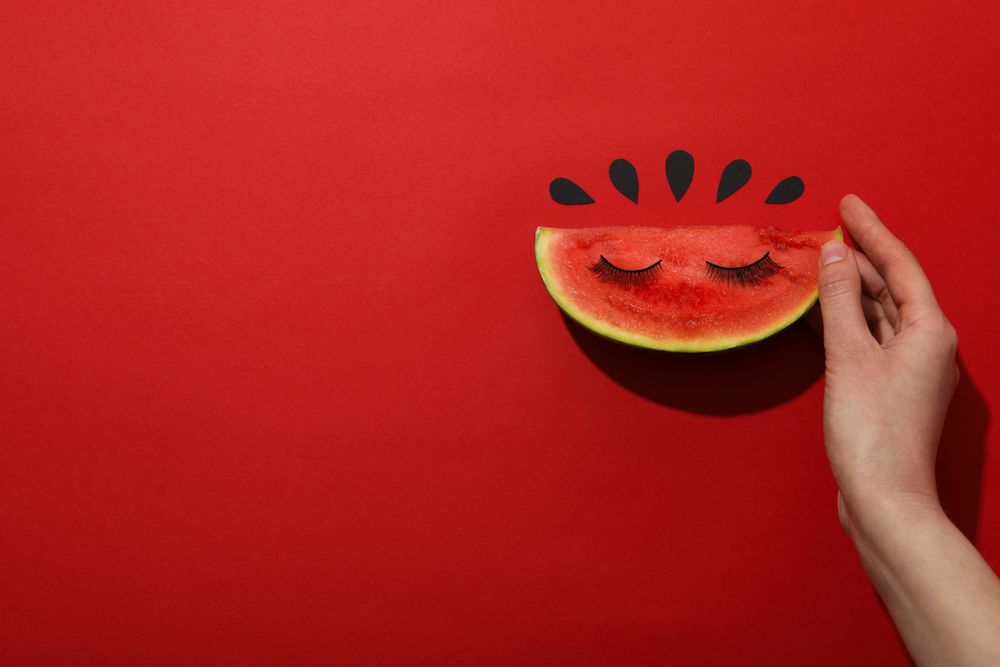 A slice of watermelon with decorative eyelashes on a red background