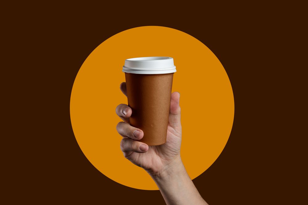 Hand holding a takeaway coffee cup on a graphic brown and orange background.