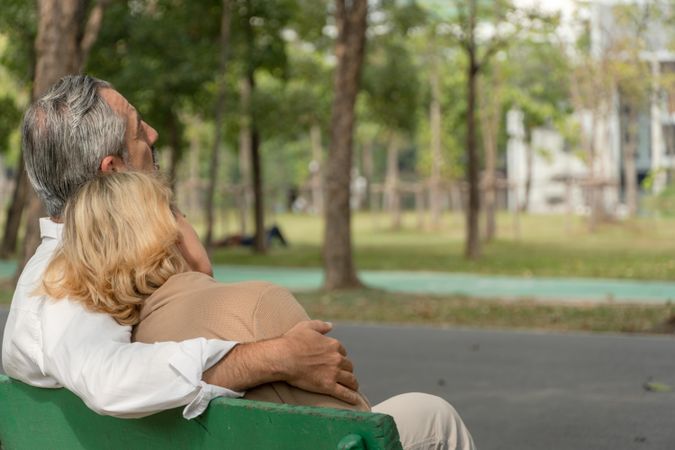 Back of male and female older couple relaxing together on park bench
