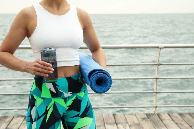 Yoga mat and bottle of water in female hands outdoors, space for text