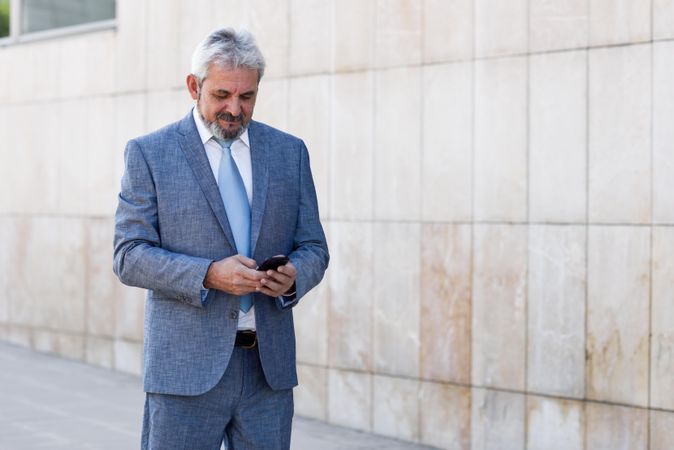 Grey haired male in formal suit checking his phone outside