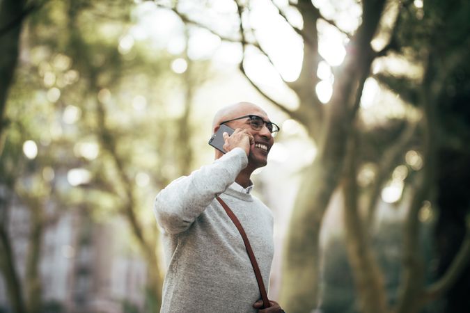 Man walking through park wearing office bag talking on mobile phone