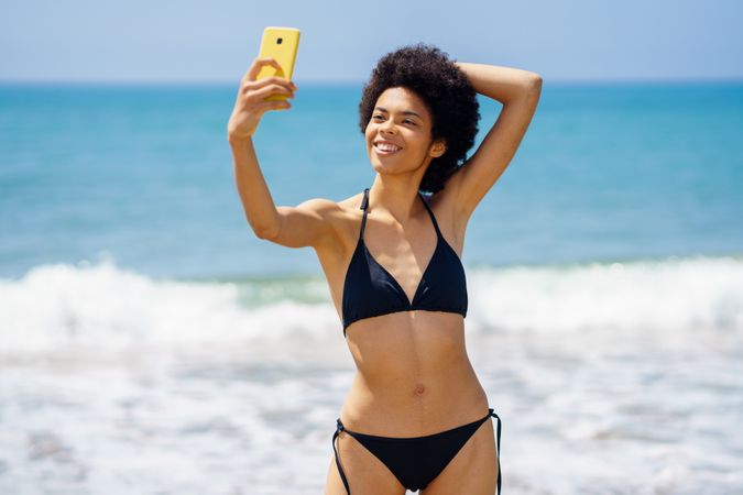 Happy woman in biking standing near the ocean taking a selfie