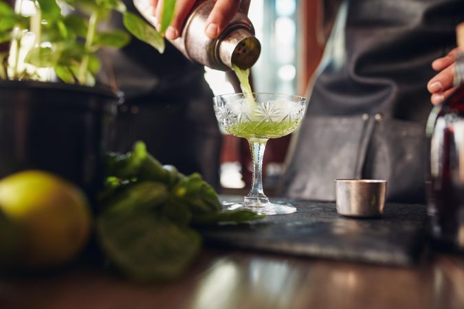 Close up shot of bartender hand pouring basil cocktail in a glass from shake