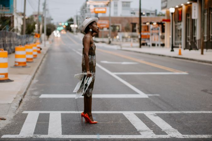 Woman standing in the crosswalk wearing red heels holding a newspaper