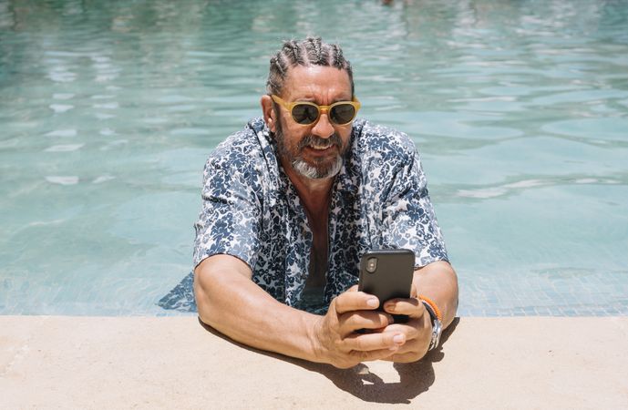Grey haired man using smartphone in swimming pool