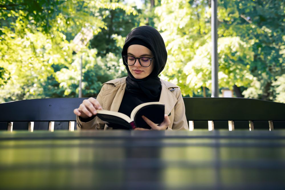 Woman reading a novel at a park table on a sunny day