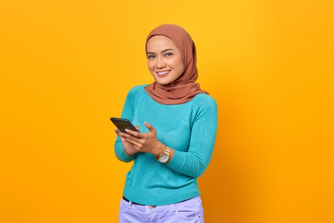 Smiling Muslim woman holding her smartphone