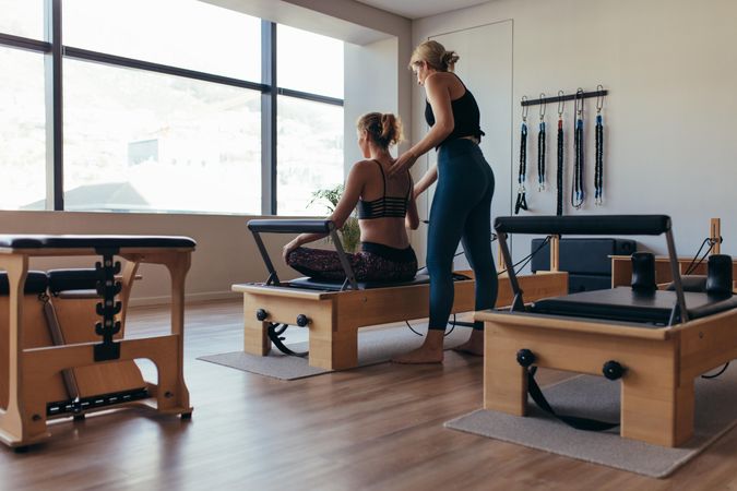Rear view of a trainer guiding a woman doing pilates workout at the gym