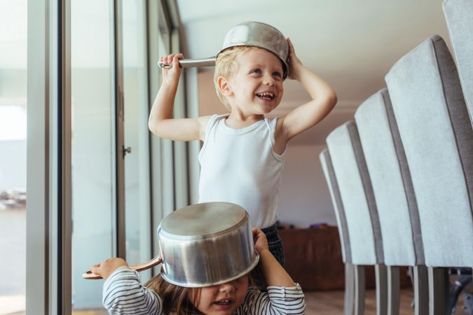 Smiling young boy and girl wearing bowls as helmet at home