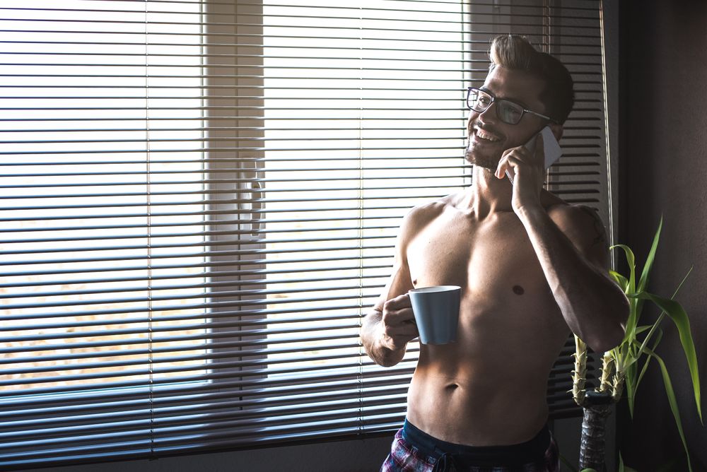 Man standing by a windows blind speaking on the mobile phone