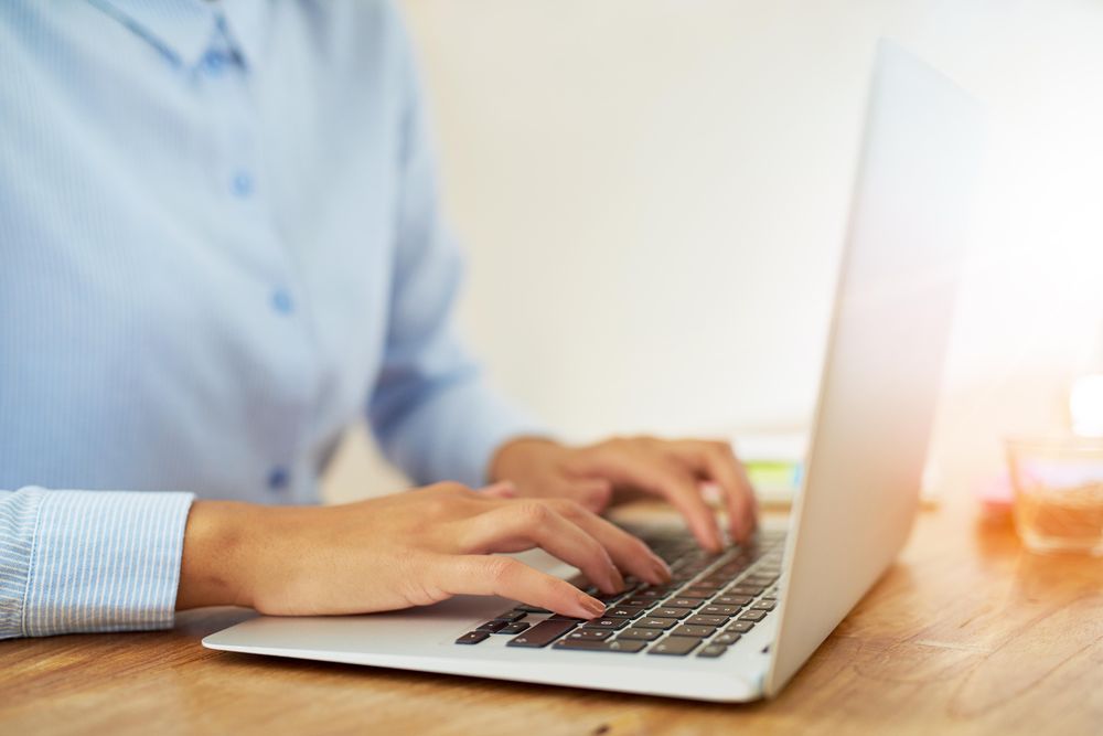 Side view of female hands in blue shirt typing on laptop
