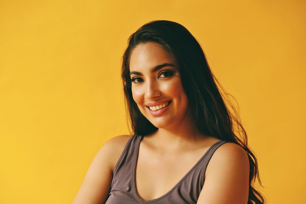 Smiling Hispanic woman looking at camera in yellow room, copy space