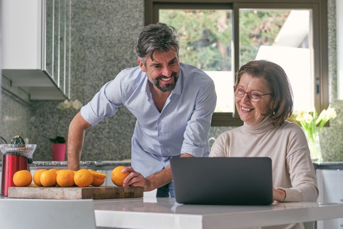 Cheerful man with senior mother using laptop in kitchen