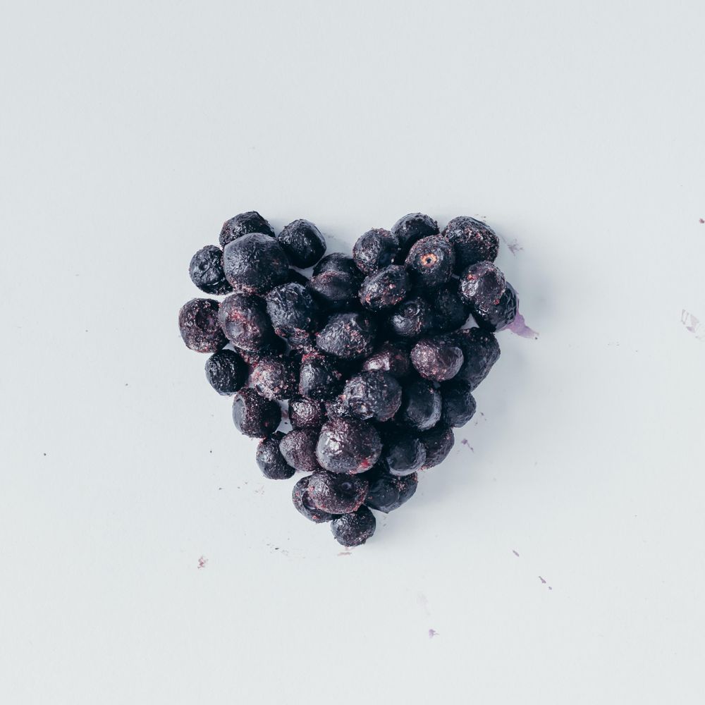 Heart shape made of frozen blueberries on light background