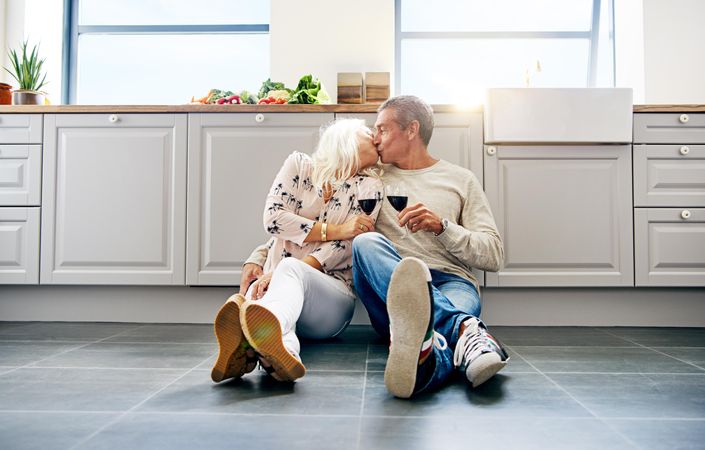 Older couple kissing and toasting with red wine on kitchen floor