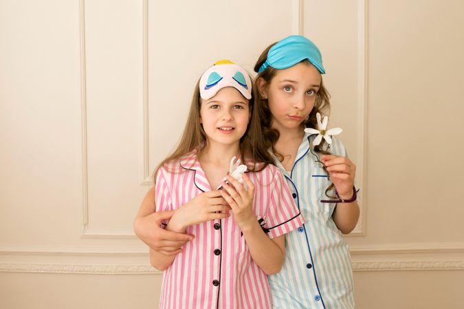 Girls in striped pajamas wearing sleep masks holding flowers