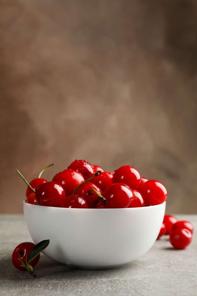 Bowl with red cherry on gray table, space for text