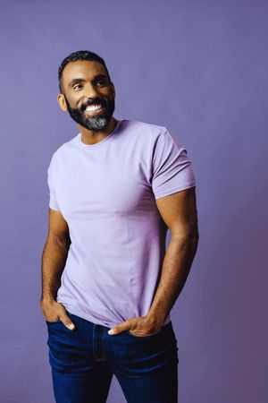 Smiling male in purple studio with hands in pocket, vertical